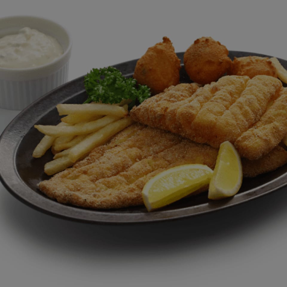 Fried fish fillets, french fries, hush puppies, lemon wedges, and tartar sauce on a plate.